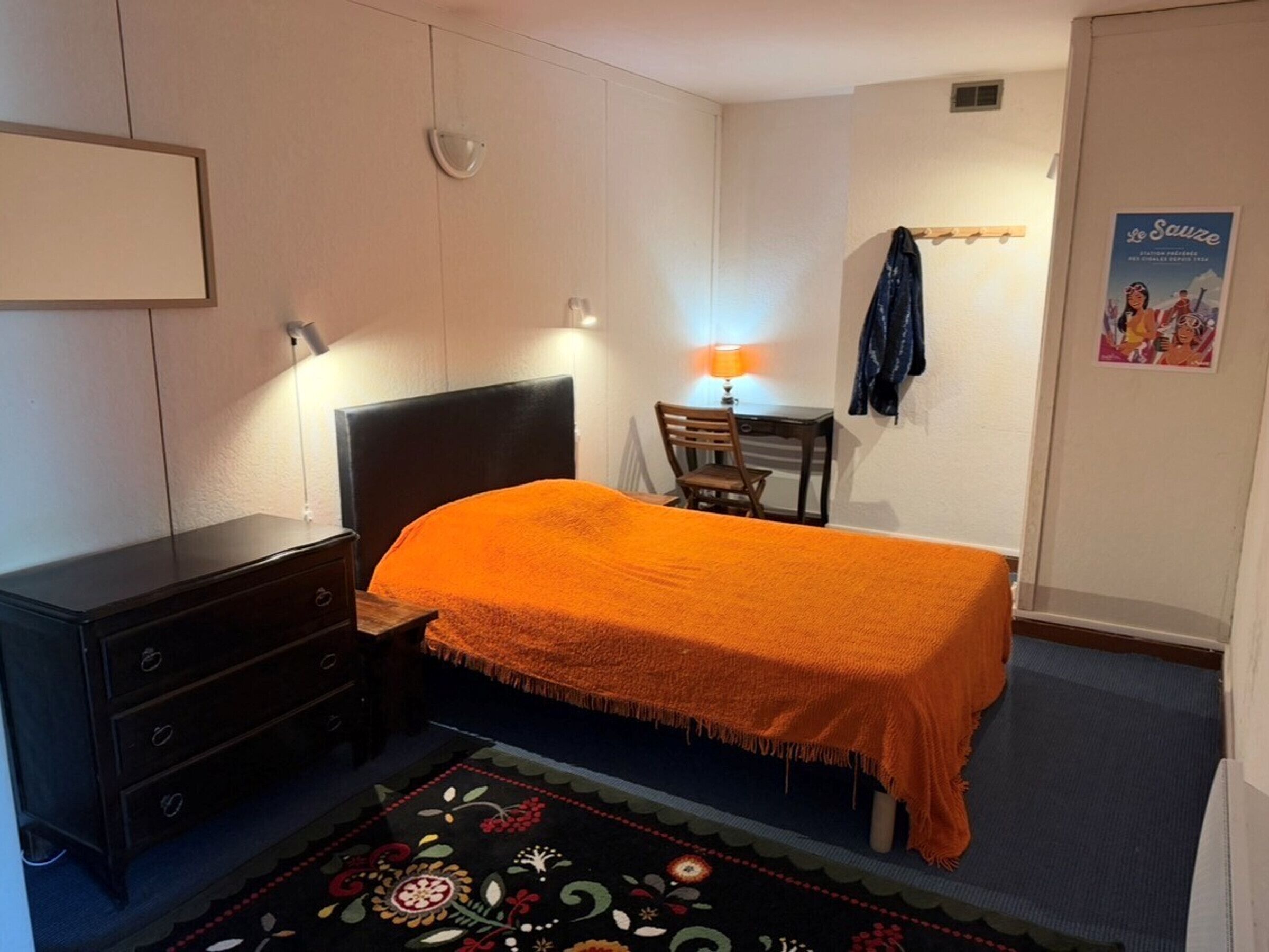 Ein Schlafzimmer mit Bett, Schreibtisch, Stuhl, Kommode und einem Bild an der Wand.