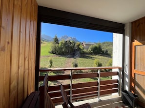 A balcony with a wooden railing, a view of a mountain, and a building in the distance. - Spacious T2 facing slopes - 6 pers, South, Comfort (Enchastrayes)