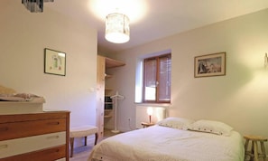 A bedroom with a bed, a dresser, a chair, a wardrobe, a radiator, and a window with blinds.