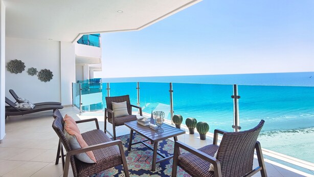 A balcony with wicker furniture, a glass railing, and a view of the ocean.