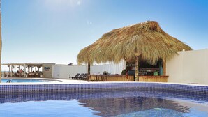 A pool area with a thatched umbrella, lounge chairs, and a bar.