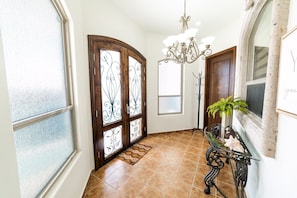 A hallway with a glass door, a chandelier, and a potted plant.
