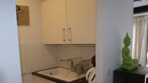 A kitchen with white cabinets, a stainless steel sink, and a green Buddha statue on a black surface. - Charming Villa with Terrace, A/C, near Tantra Club, Private Parking (Cap d'Agde naturisme)