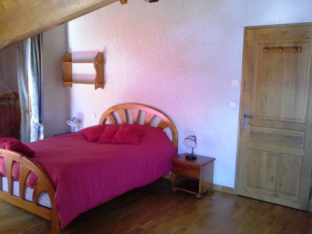 A bedroom with a wooden bed, a nightstand, a wooden door, and a window with curtains.