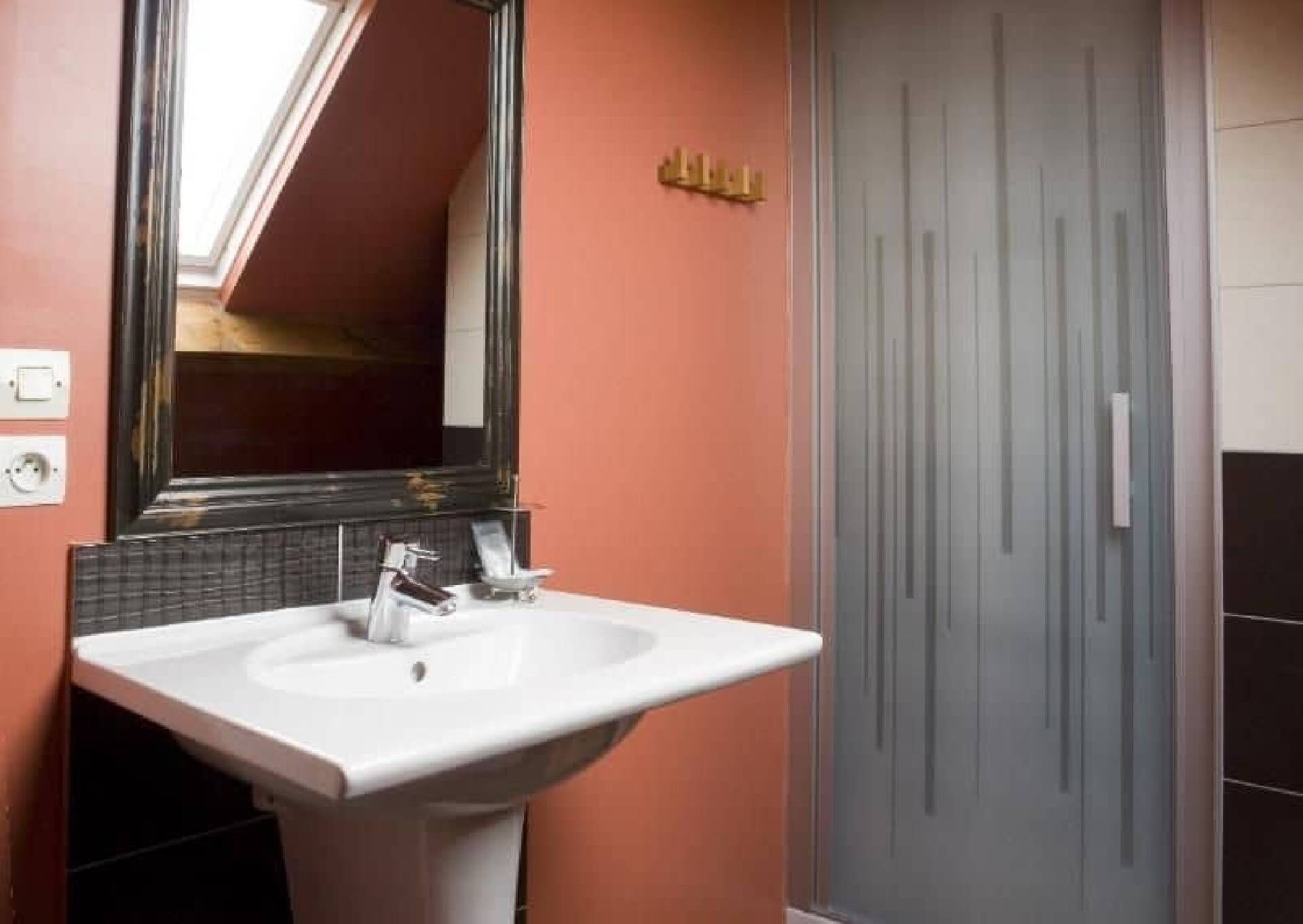Une salle de bain avec un lavabo blanc, un grand miroir et une porte ornée de lignes verticales.
