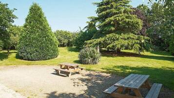 A picnic area with two wooden tables and benches, surrounded by well-maintained grass and trees.