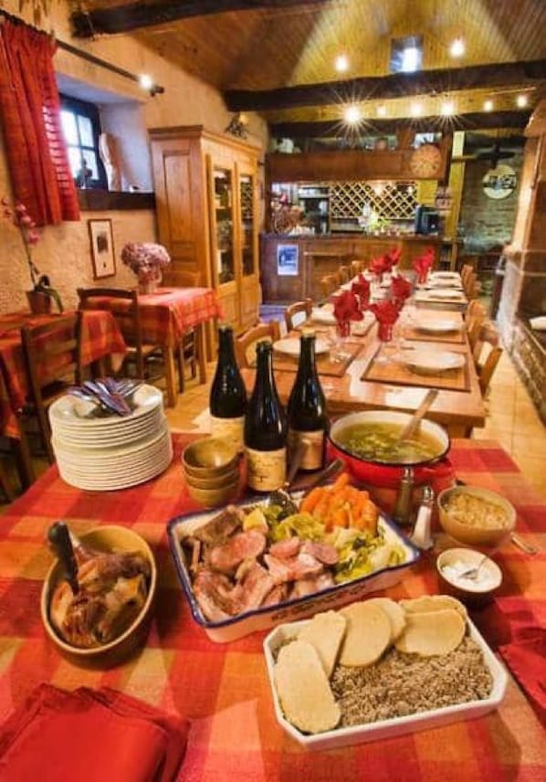 Un espace repas avec une longue table dressée pour un repas, où l’on peut voir différents plats et bouteilles.