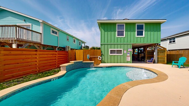 Une piscine avec une terrasse en bois, une clôture en bois et une serre visible au fond.