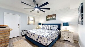 Une chambre à coucher avec un lit, un ventilateur de plafond, une fenêtre, un tableau et une table de chevet.