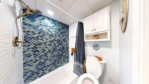 Une salle de bain équipée d’une douche, de toilettes et d’un meuble contenant des objets décoratifs.