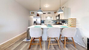 Una cucina moderna con isola centrale, due sgabelli da bar, illuminazione a sospensione e frigorifero in acciaio inossidabile.