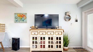 Un salon avec un téléviseur posé sur un meuble en bois, un tableau, un objet décoratif et une plante.