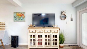 A living room with a TV on a wooden cabinet, a painting, a decorative sign, and a plant.