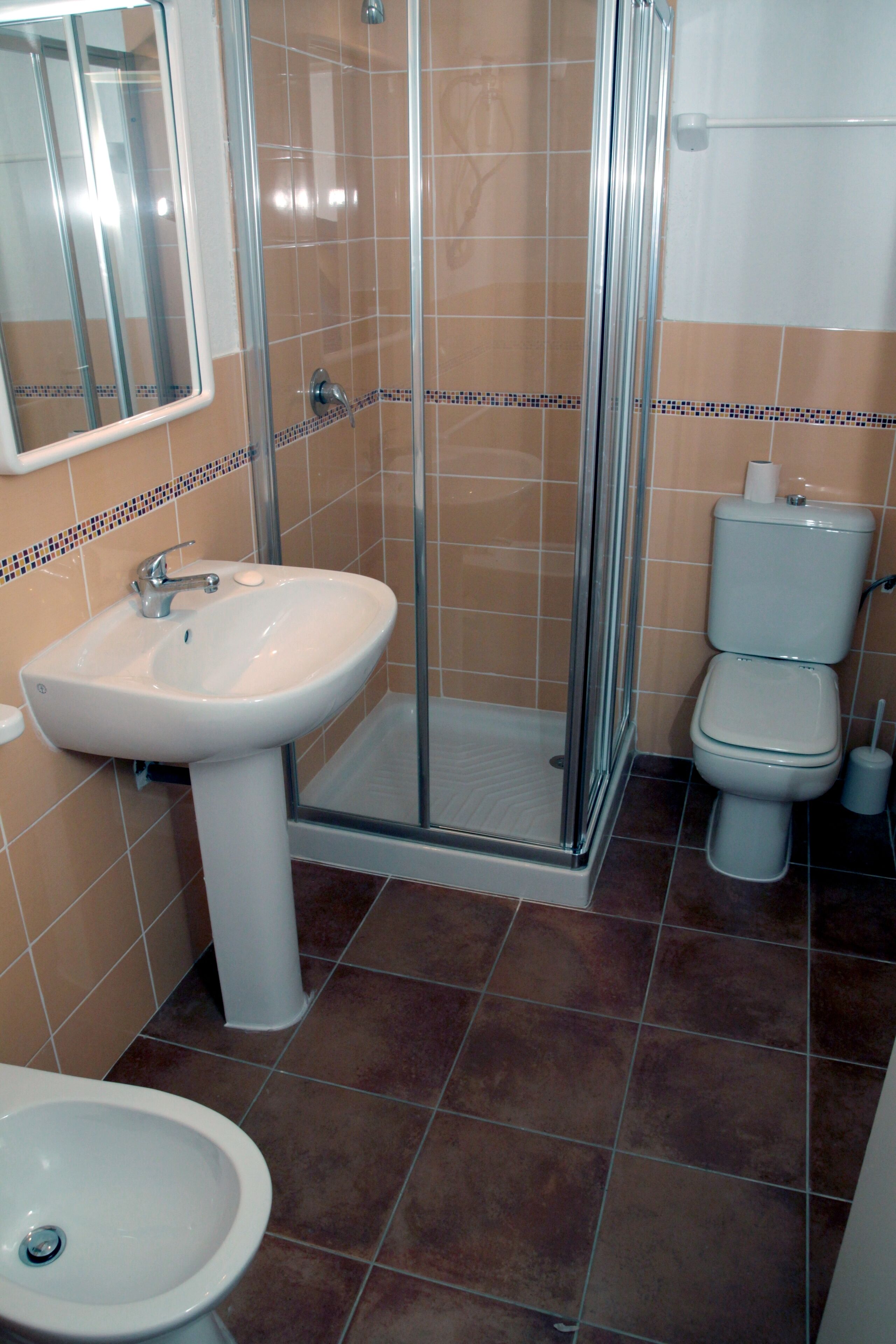 A bathroom with a glass-enclosed shower, a pedestal sink, a toilet, and a bidet.