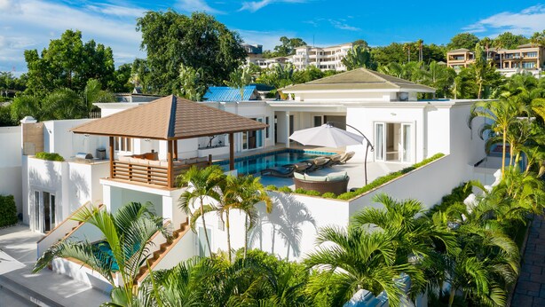 Ett modernt hus med en swimmingpool, en täckt uteplats och frodig grönska.