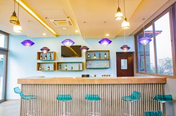A modern bar area with a wooden counter, green bar stools, pendant lighting, and shelves with bottles. - Royal Residences by Design Union (Lagos)