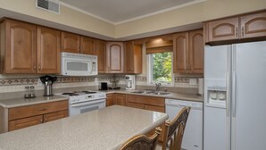 Una cocina con armarios de madera, un microondas blanco, una estufa, un fregadero y un refrigerador.