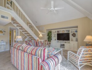 A spacious living room with a striped sofa, a flat-screen TV, and a staircase.
