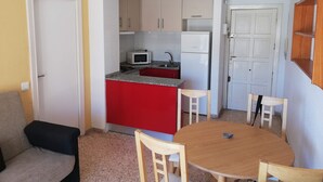 Kompakti keittiö, jossa on punainen keittiösaareke, mikroaaltouuni ja jääkaappi. Olohuoneessa on ruokapöytä neljällä tuolilla sekä sohva.
