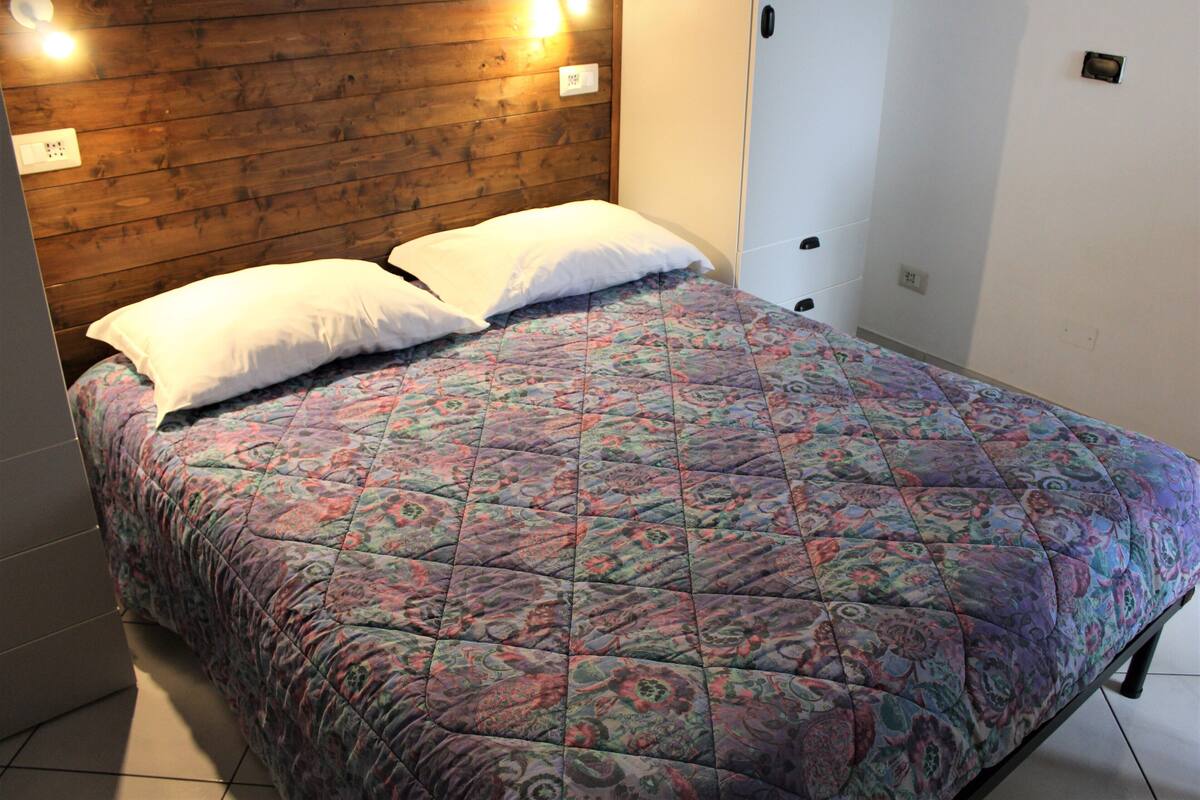 A bed with a floral-patterned quilt, two white pillows, and a wooden headboard with wall-mounted lights.
