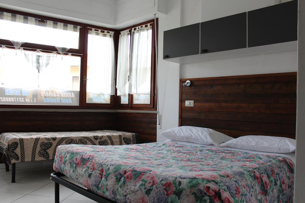 A bedroom with a wooden headboard, a floral bedspread, a bedside table with a patterned tablecloth, and a window with curtains.