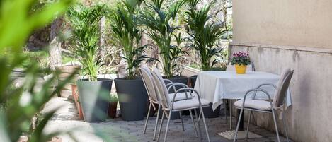 Een terras buiten, met een tafel en stoelen, omringd door plantenpotten.