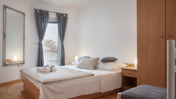 Una cama bien hecha con almohadas y una manta, un armario de madera, una silla y una ventana con cortinas.