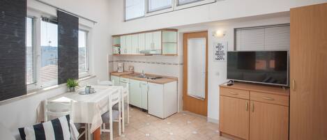 A compact kitchen with a dining area, a TV, and a window with blinds.