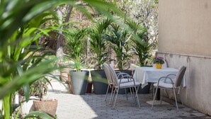 Un patio al aire libre con una mesa y sillas, rodeado de grandes macetas con plantas y un muro de concreto.