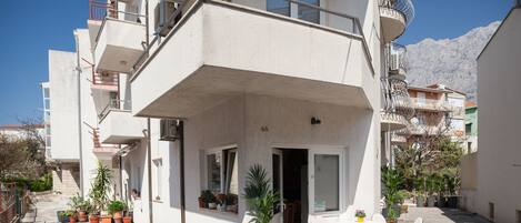 A multi-story residential building with balconies, a patio area with outdoor seating, and potted plants.