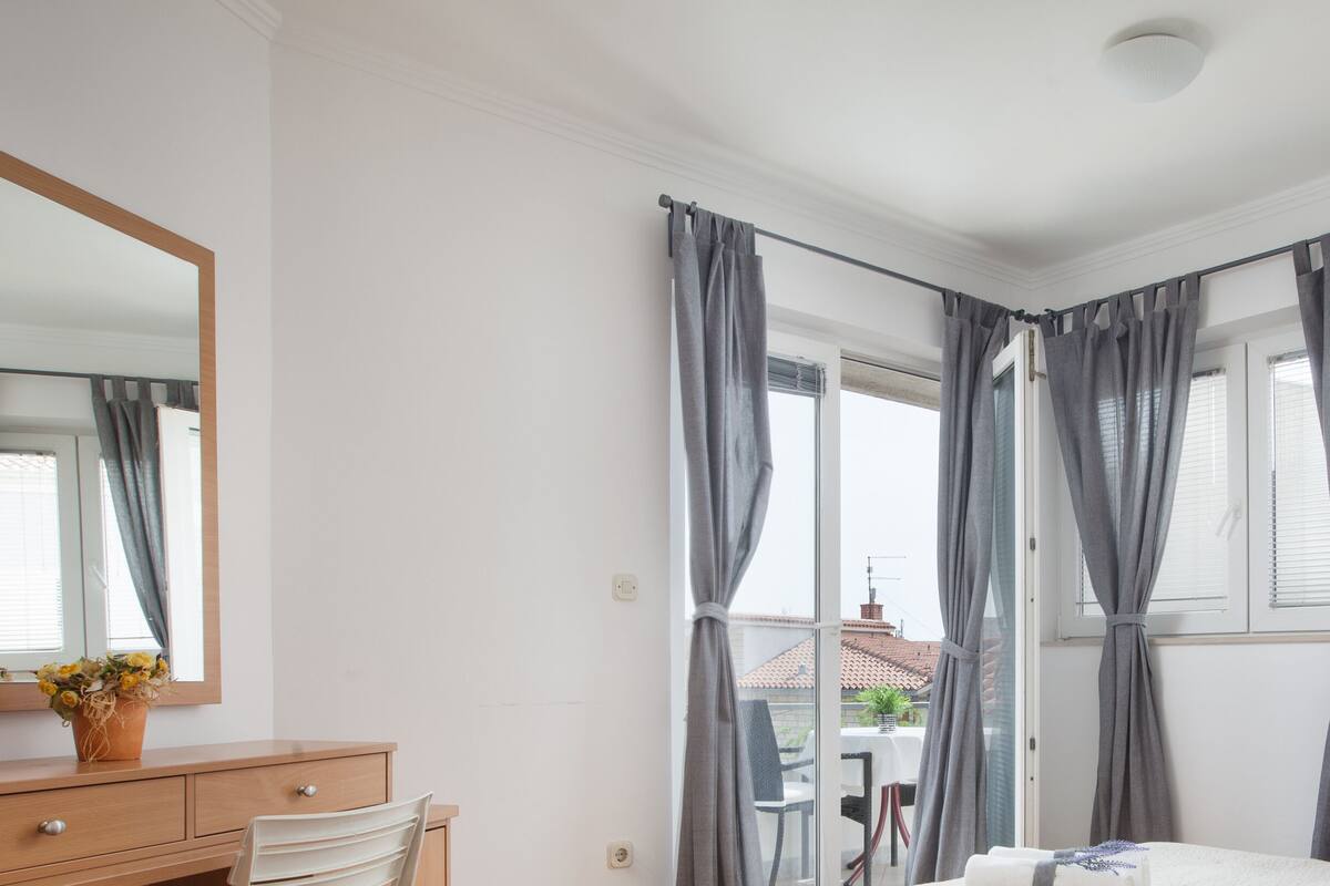 A bedroom with a bed, a dresser, a mirror, and a window with curtains.