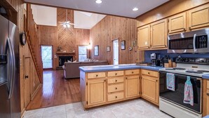 A modern kitchen with wooden cabinetry, a large island, stainless steel appliances, and a view into the living area. - A Some Place Special Minutes to Beach Sleeps 10 (Pawleys Island)