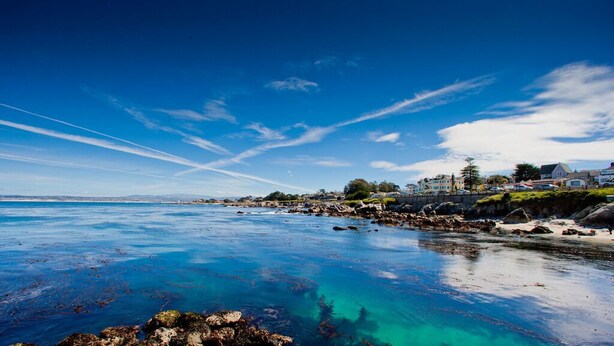 A coastal area with clear blue waters, rocky shorelines, and buildings on the right side. - Fourth Tee - Pacific Grove House - Ocean/Golf View (Pacific Grove)