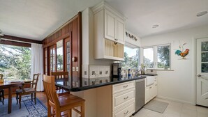 A kitchen with wooden cabinets, a black countertop, and a dining area with a table and chairs. - Fourth Tee - Pacific Grove House - Ocean/Golf View (Pacific Grove)