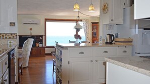 A kitchen with white cabinets, a wooden floor, and a view of the sea through a large window. - The View: The Name Says It All (Rockport)