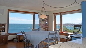 A dining area with a table and chairs, large windows with a view of the sea, and a hanging light fixture. - The View: The Name Says It All (Rockport)