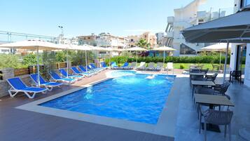 Una piscina con sillones reclinables azules y blancos, una mesa con sillas y sombrillas.