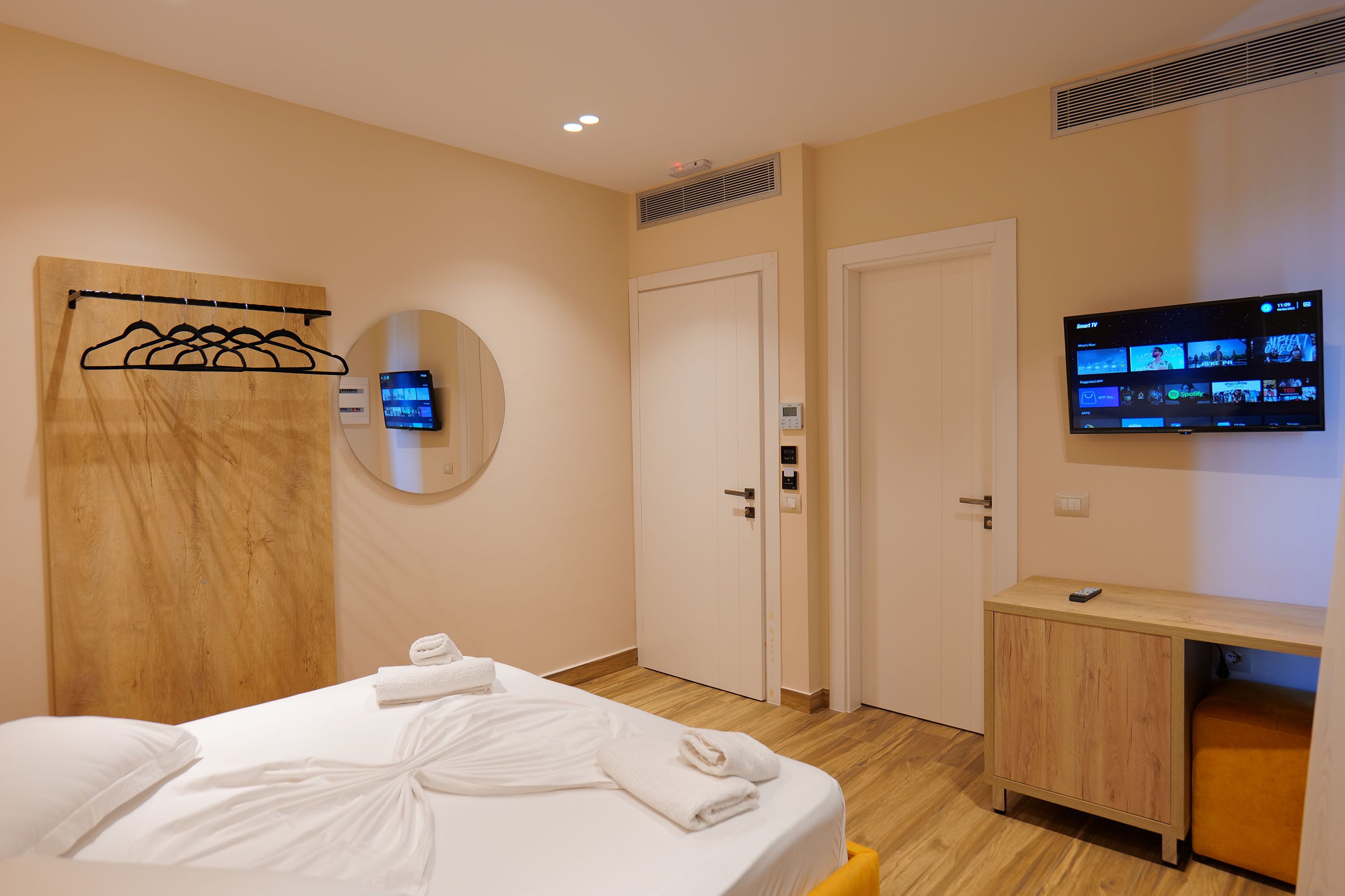 Una habitación de hotel con una cama, cabecera de madera, televisor montado en la pared y un mueble de madera.