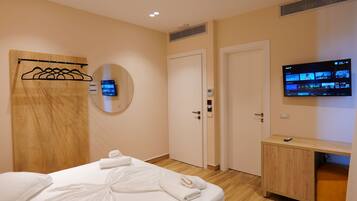 Una habitación de hotel con una cama, cabecera de madera, televisor montado en la pared y un mueble de madera.