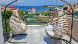 Two wicker swing chairs with white cushions on a balcony overlooking a coastal town. - Hotel Alexander (Ksamil)