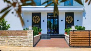 A modern hotel entrance with a stone wall, wooden bench, and potted plants. - Hotel Alexander (Ksamil)