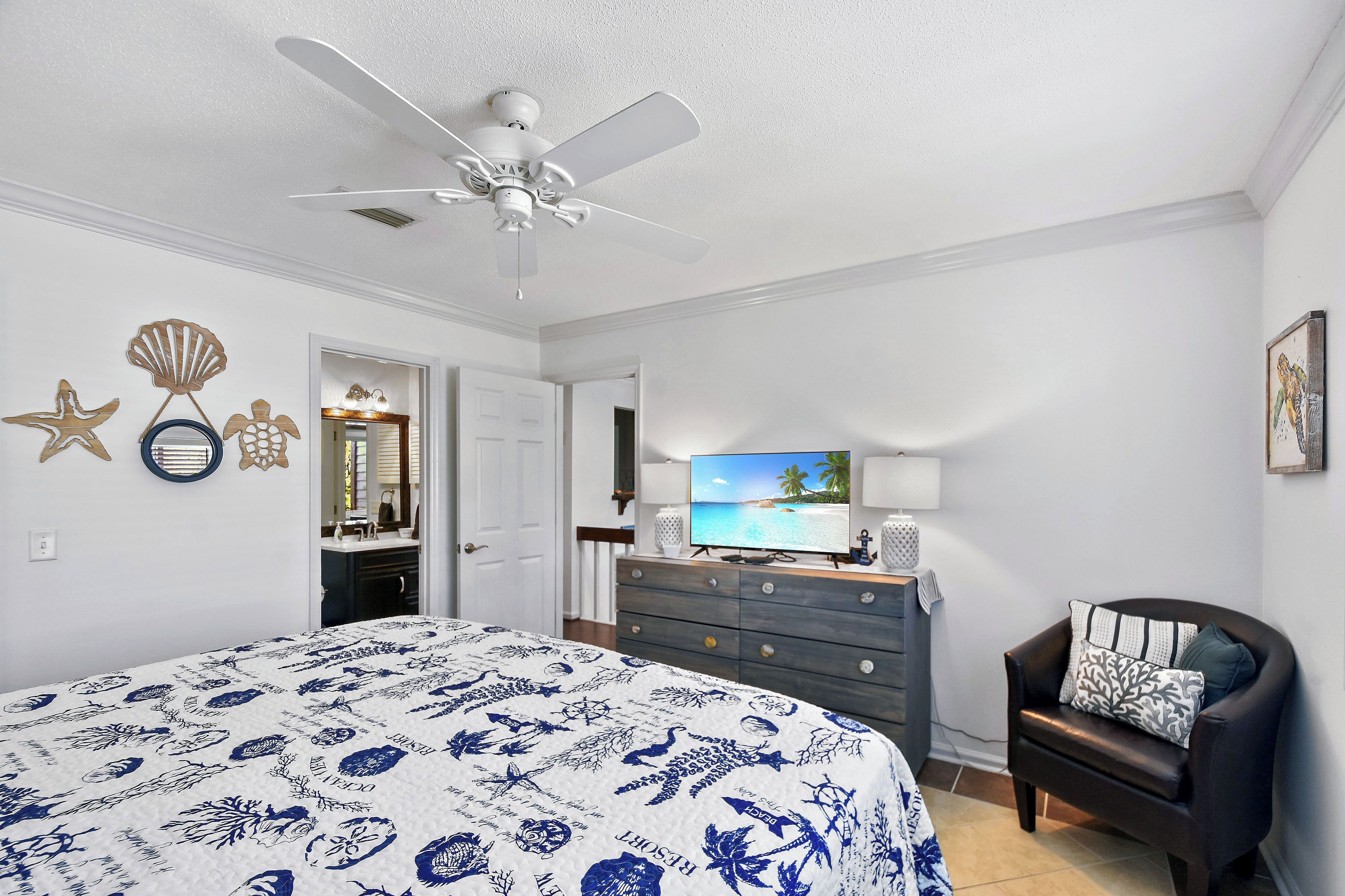 A bedroom with a bed, a ceiling fan, a dresser, a TV, and a chair.