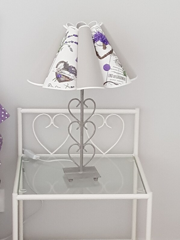 A white metal lamp with a heart-shaped design on the backrest and a decorative lampshade with purple floral patterns. - Gîte La Volière (Cardet)