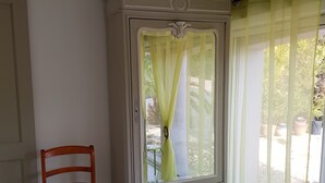 Ein Zimmer mit einem Holzsessel, einem weißen Schrank mit Spiegel und einem Fenster mit gelben Vorhängen.