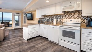 A modern kitchen with white cabinets, a microwave, a stove, and a large window overlooking a balcony. - High Point South 1C-Oceanfront 112th St, WIFI, Pool, Elev, W/D, AC (Ocean City)