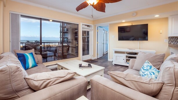 A living room with a large sliding glass door leading to a balcony, a ceiling fan, a flat-screen TV, and a white entertainment unit. - High Point South 1C-Oceanfront 112th St, WIFI, Pool, Elev, W/D, AC (Ocean City)
