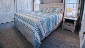 A bedroom with a large bed, two bedside tables, a wardrobe, and a window with curtains. - Stunning Renovations, Top Floor Views, and less than 2 Blocks to the Beach! (Wildwood)
