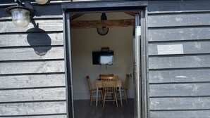 A wooden building with a dining area featuring a table and chairs, a clock on the wall, and a sign indicating the name of the place.