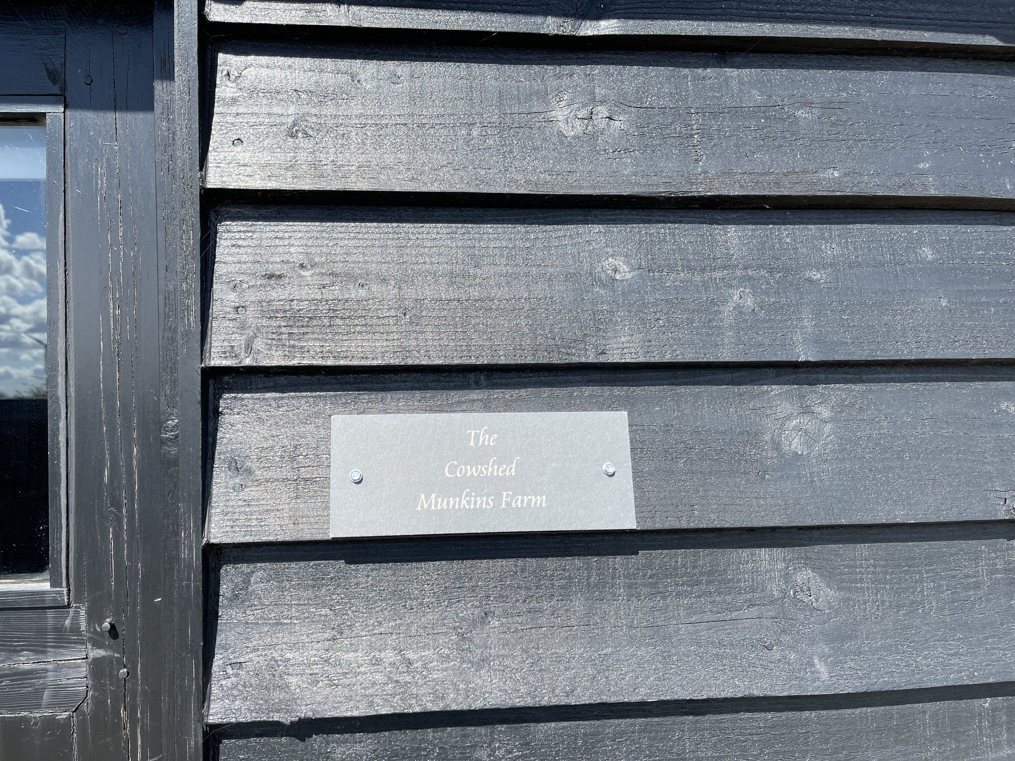A metal plaque on a wooden wall with the text "The Cowshed Munkins Farm".