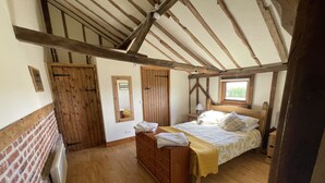 A bedroom with a wooden ceiling, a bed with white bedding, a wooden dresser, and a window.